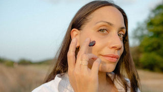 Woman applies Apoterra's Hibiscus Exfoliating Mud Mask on her cheek