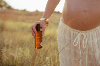 Maternity skincare oil held by pregnant woman in field