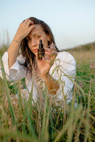 Woman holding skincare bottle in field (0U1A4899)