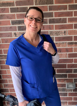 Woman in blue scrubs smiling in front of brick wall