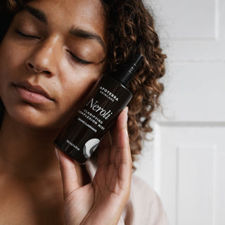 Neroli Clarifying Mist by Apoterra spray bottle is being held near a model's face relaying the benefits of clear skin, & brightened complexion 