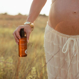 Vitamin C Body Oil - Classic Unscented is held by a pregnant woman in an outdoor lifestyle image