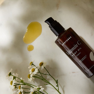 Apoterra Unscented Classic Vitamin C Body Oil lifestyle image showing oil texture with chamomile flowers